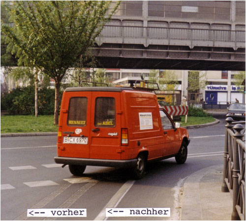 Foto: Neue Markierung des Radfahrstreifens Adalbertstraße in Berlin - ein Zollstock zeigt, dass die neue Breite 1m beträgt, die alte Breite von 2m ist an den Ausfräsungen im Asphalt noch sichtbar. Ein Auto schneidet die Kurve, so dass noch ca. 0,5m zwischen Bordstein und Fahrzeug verbleiben. 