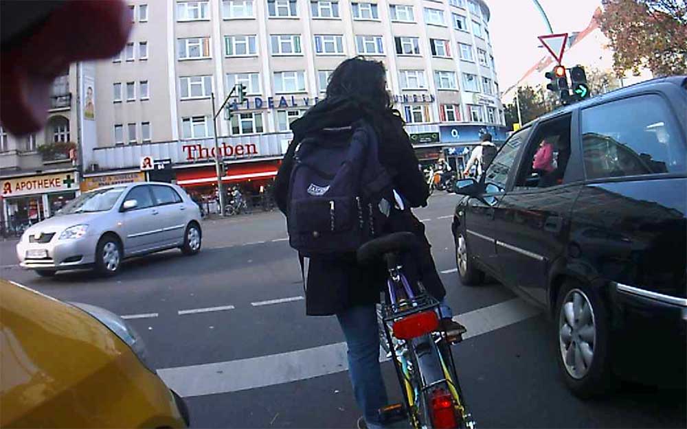 Foto: Radfahrerin in der Linksabbiegesur mit dicht vorbeifahrenden Pkw in der rechten Spur.